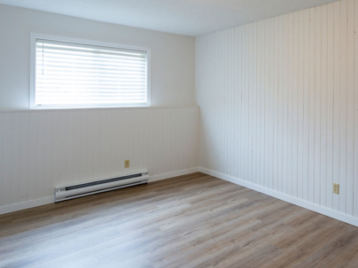 an empty room with a window, wood-paneled walls, and what appears to be a baseboard heater installed below the window.